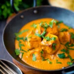 Paneer tikka masala curry served in an iron karai with naan bread.
