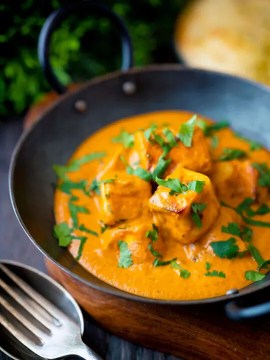 Paneer tikka masala curry served in an iron karai with naan bread.