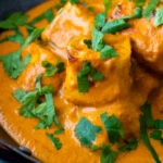 Close up paneer tikka masala curry served in an iron karai with naan bread.