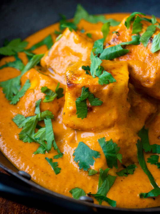 Close up paneer tikka masala curry served in an iron karai with naan bread.