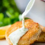 White parsley sauce poured from a jug over a fishcake.