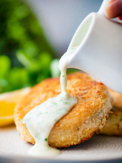 White parsley sauce poured from a jug over a fishcake.
