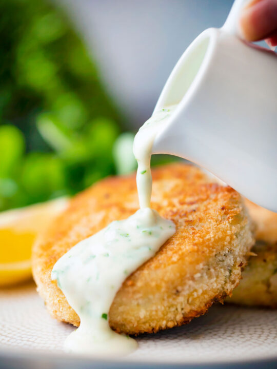 White parsley sauce poured from a jug over a fishcake.