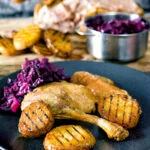 Roast duck leg served with duck fat potatoes and red cabbage.