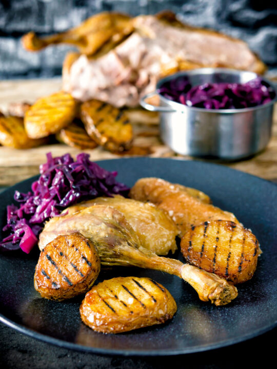 Roast duck leg served with duck fat potatoes and red cabbage.