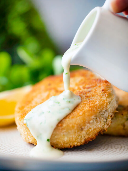 Smoked haddock fishcakes with parsley sauce being poured over them.