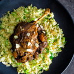 Overhead tamarind duck leg with a date and almond sauce served with couscous featuring a title overlay.