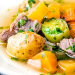 Close up Welsh cawl, a lamb and vegetable broth based soup in a white bowl.