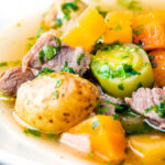 Close up Welsh cawl, a lamb and vegetable broth based soup in a white bowl featuring a title overlay.