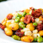 Fried chorizo gnocchi with broad beans, peas and manchego cheese served in a white bowl.