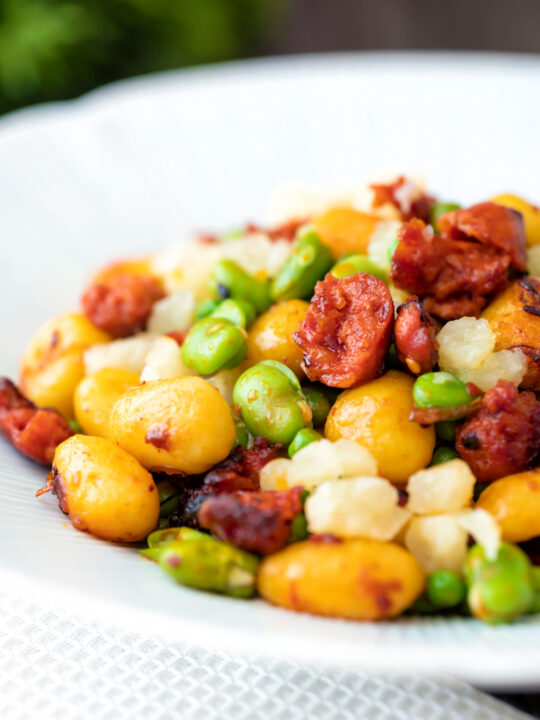 Fried chorizo gnocchi with broad beans, peas and manchego cheese served in a white bowl.