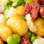 Close up chorizo gnocchi with green peas and broad beans.