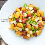 Overhead chorizo gnocchi with green peas, broad beans and manchego cheese featuring a title overlay.