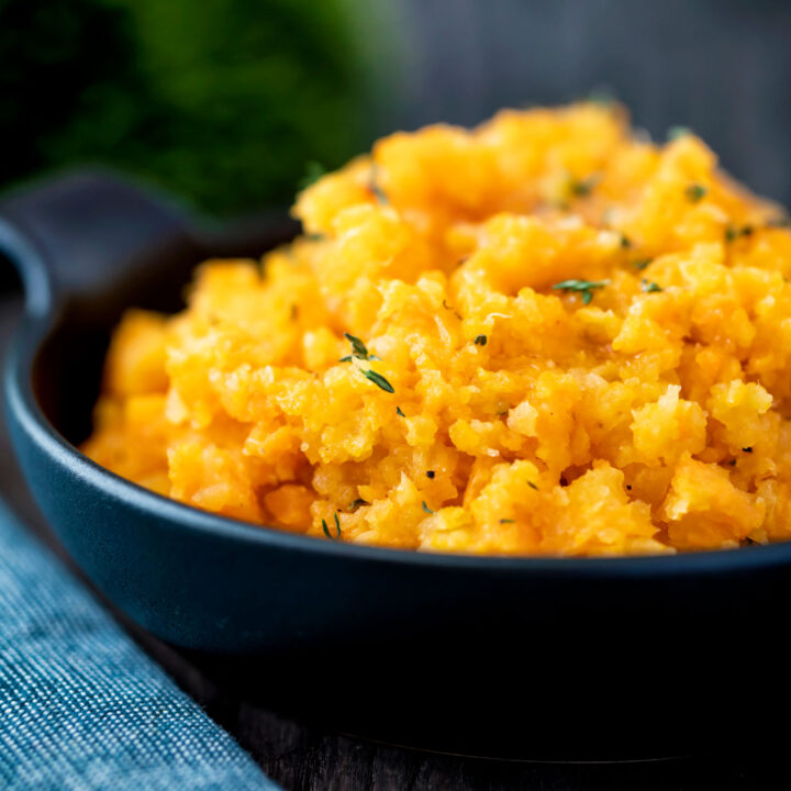 Swede and carrot mash with fresh thyme served in a black bowl.
