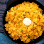 Overhead swede and carrot mash with a knob of butter in a black bowl.