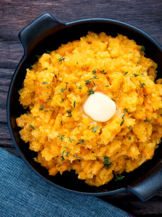 Overhead swede and carrot mash with a knob of butter in a black bowl.