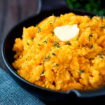 Swede and carrot mash with a knob of butter in a black bowl.