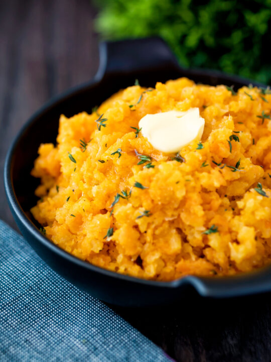 Swede and carrot mash with a knob of butter in a black bowl.