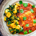 Overhead aloo methi or fenugreek potatoes served with a cod curry featuring a title overlay.