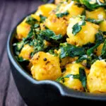 Close up aloo methi or fenugreek potatoes served in a black dish.
