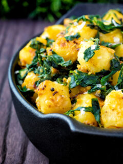 Close up aloo methi or fenugreek potatoes served in a black dish.