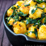 Close up aloo methi or fenugreek potatoes served in a black dish featuring a title overlay.