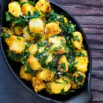 Overhead aloo methi or fenugreek potatoes served in a black dish.