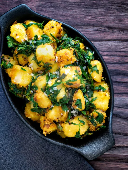 Overhead aloo methi or fenugreek potatoes served in a black dish.