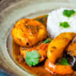 Close up aloo paneer or chanar dalna served in a bowl with rice and coriander.