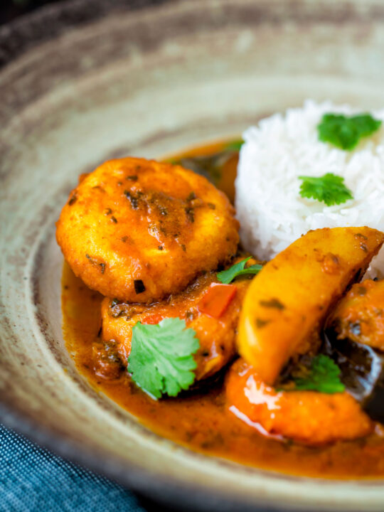 Close up aloo paneer or chanar dalna served in a bowl with rice and coriander.