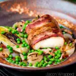 Bacon wrapped cod loin served with French braised peas and lettuce featuring a title overlay.