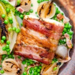 Close up bacon wrapped cod loin served with French braised peas and lettuce.