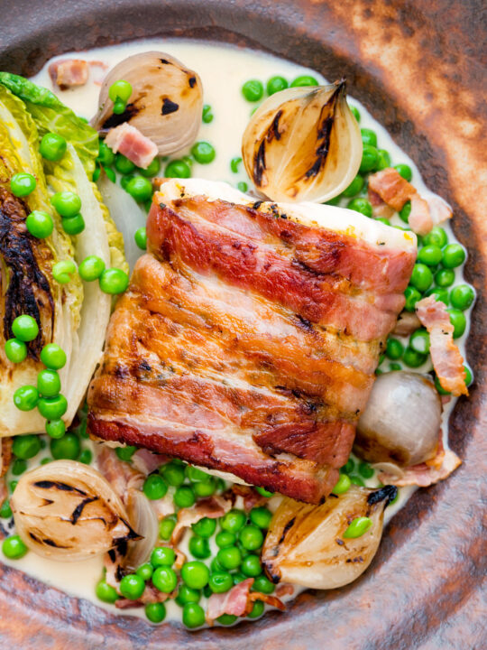 Close up bacon wrapped cod loin served with French braised peas and lettuce.