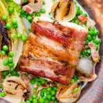 Close up bacon wrapped cod loin served with French braised peas and lettuce featuring a title overlay.