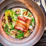 Overhead bacon wrapped cod loin served with French braised peas and lettuce.