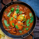 Overhead chicken rogan josh curry served in an iron karai with a naan bread.