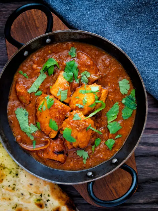 Overhead chicken rogan josh curry served in an iron karai with a naan bread.