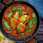 Overhead chicken rogan josh curry served in an iron karai with a naan bread featuring a title overlay.