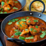 Chicken rogan josh curry served in an iron karais with a naan bread.