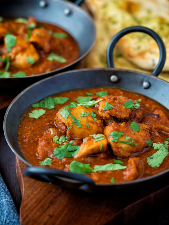 Chicken rogan josh curry served in an iron karais with a naan bread.