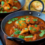 Chicken rogan josh curry served in an iron karais with a naan bread featuring a title overlay.
