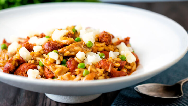 Chicken and chorizo risotto with green peas and Manchego cheese served in a white bowl.