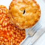 Overhead corned beef and potato pie wrapped in shortcrust pastry served with baked beans.