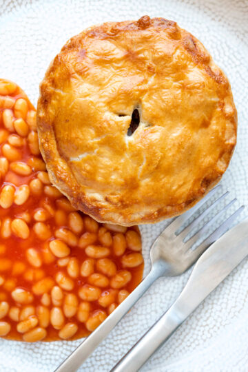 Overhead corned beef and potato pie wrapped in shortcrust pastry served with baked beans.