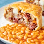 Cut open corned beef and potato pie wrapped in shortcrust pastry served with baked beans.