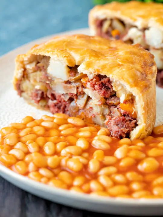 Cut open corned beef and potato pie wrapped in shortcrust pastry served with baked beans.