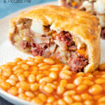 Cut open corned beef and potato pie wrapped in shortcrust pastry served with baked beans featuring a title overlay.