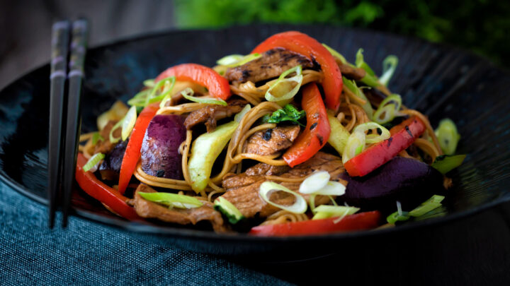 Hoisin pork stir fry with red peppers, onions and pak choi served in a dark bowl.