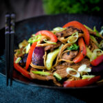 Hoisin pork stir fry with red peppers, onions and pak choi served in a dark bowl.