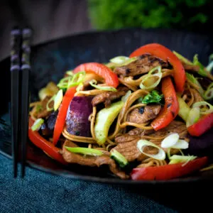 Hoisin pork stir fry with red peppers, onions and pak choi served in a dark bowl.